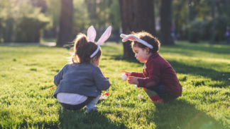 Two small children are searching for eggs. They're wearing bunny ears.